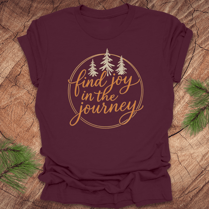 Maroon t-shirt with 'find joy in the journey' text and trees on a wooden surface.