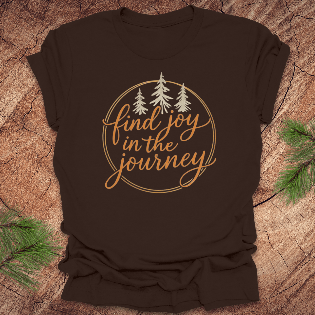 Brown t-shirt with 'find joy in the journey' text and trees on a wooden surface.