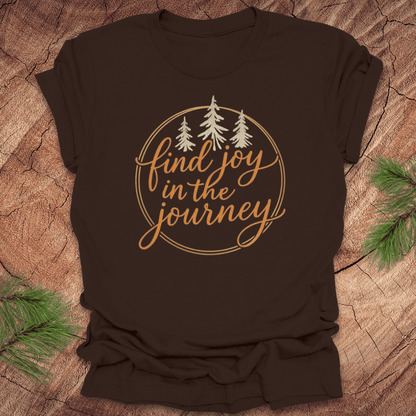 Brown t-shirt with 'find joy in the journey' text and trees on a wooden surface.