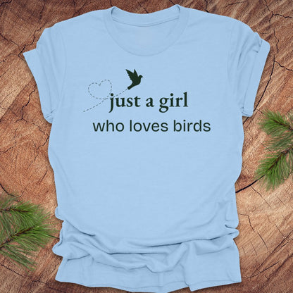 Light blue t-shirt with 'just a girl who loves birds' text on a wooden surface.