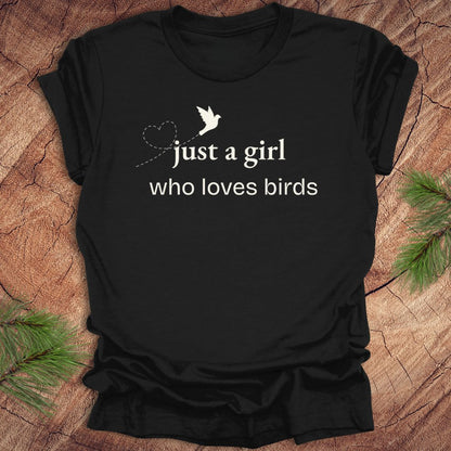 Black t-shirt with 'just a girl who loves birds' text and bird graphic on a wooden surface.