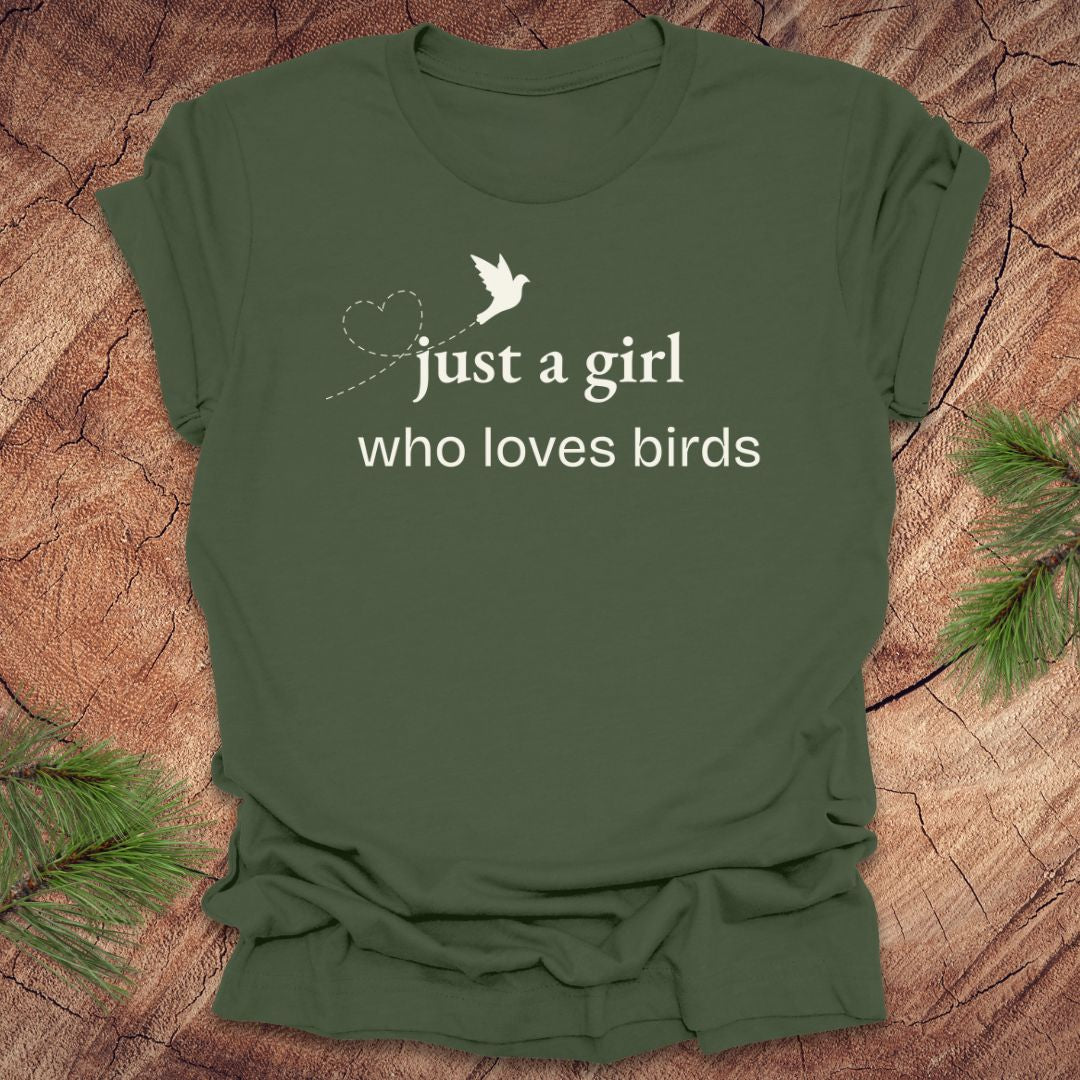 Green t-shirt with 'just a girl who loves birds' text on a wooden surface with pine branches.