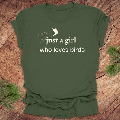 Green t-shirt with 'just a girl who loves birds' text on a wooden surface with pine branches.