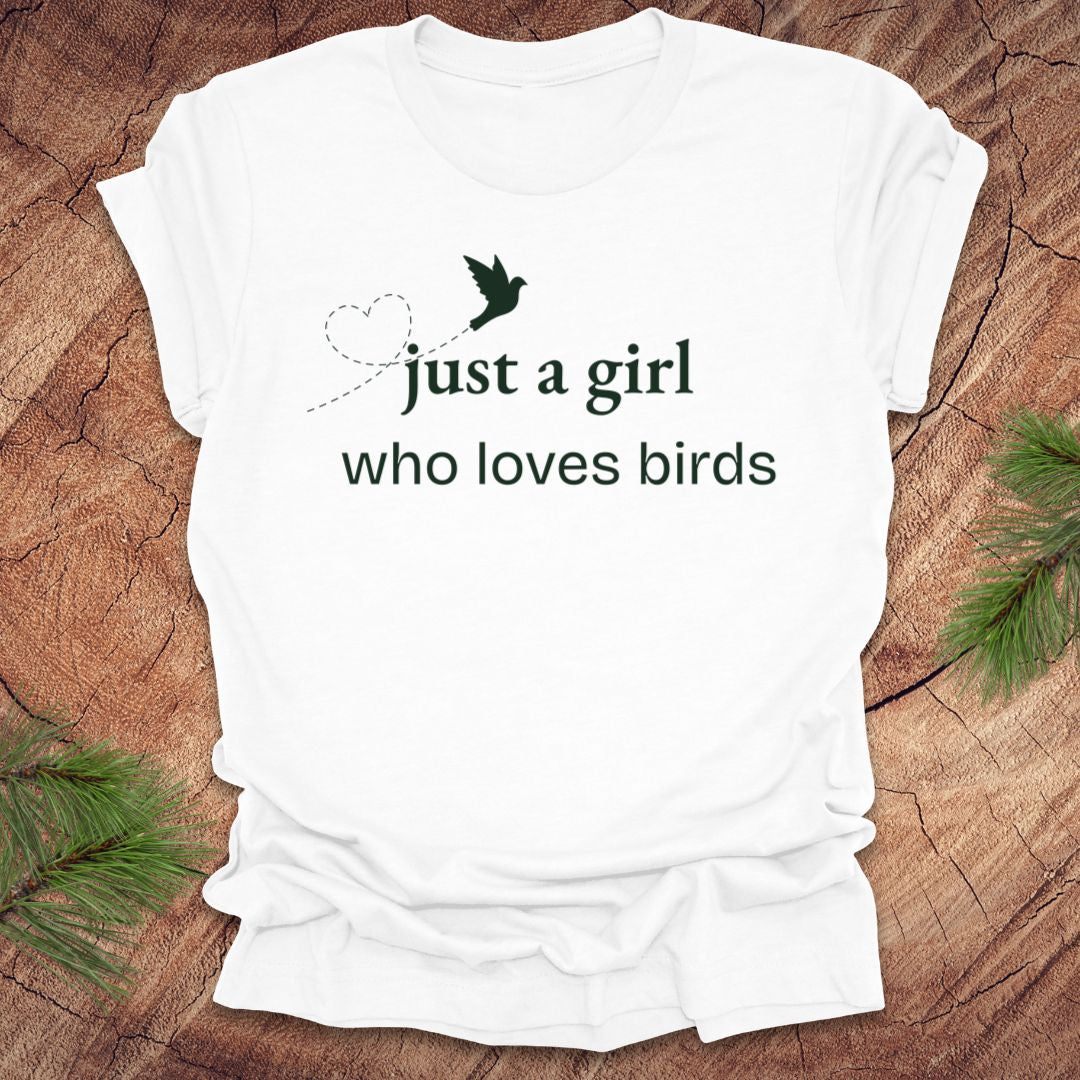 White t-shirt with 'just a girl who loves birds' text on a wooden surface with greenery.
