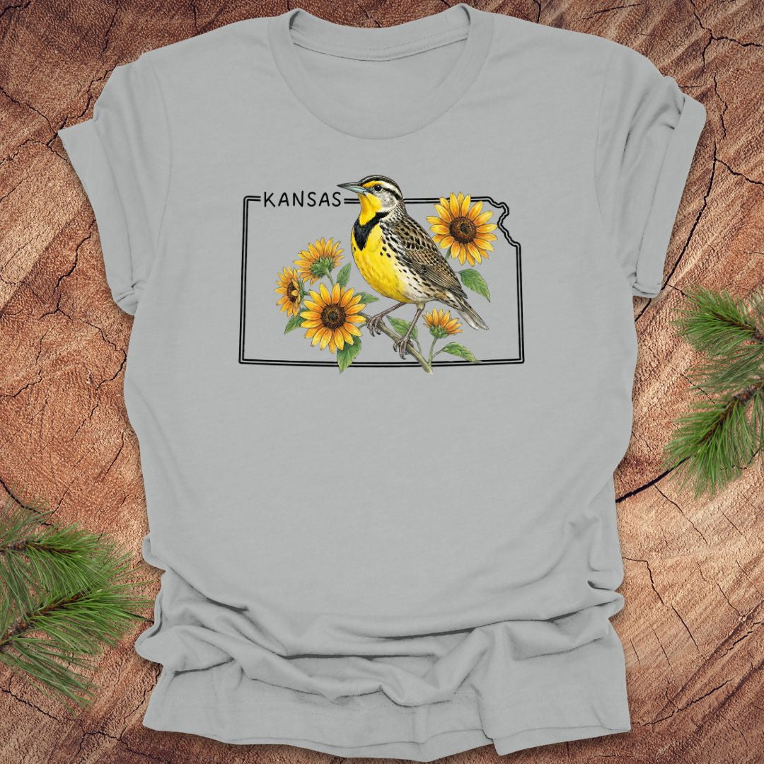 Gray t-shirt with a graphic of a bird and sunflowers on a Kansas map, placed on a wooden surface.