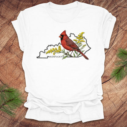 White t-shirt with the outline of the state of kentucky and state bird cardinal and goldenrod  design on a wooden surface
