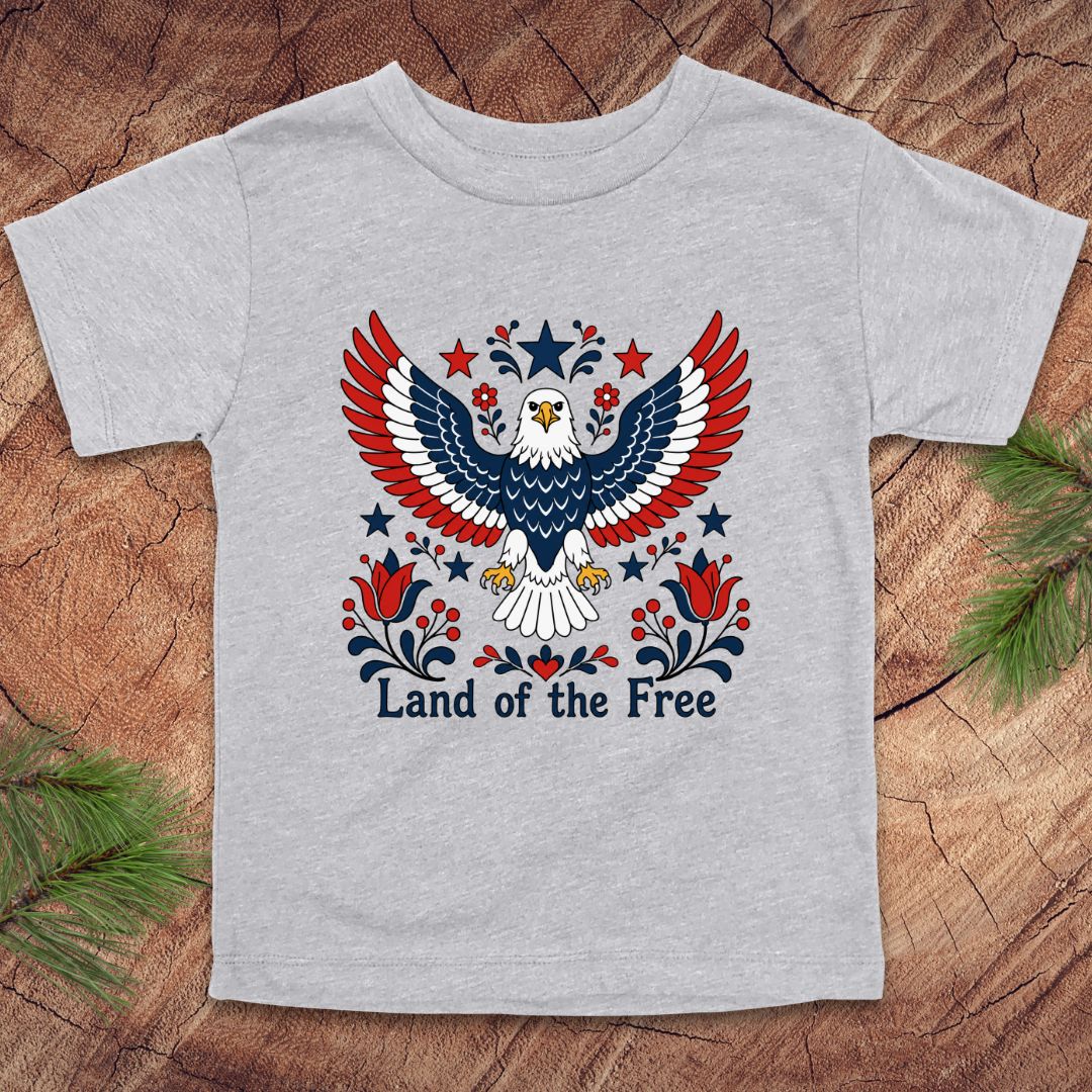 Gray t-shirt with an eagle design and 'Land of the Free' text on a wooden surface.