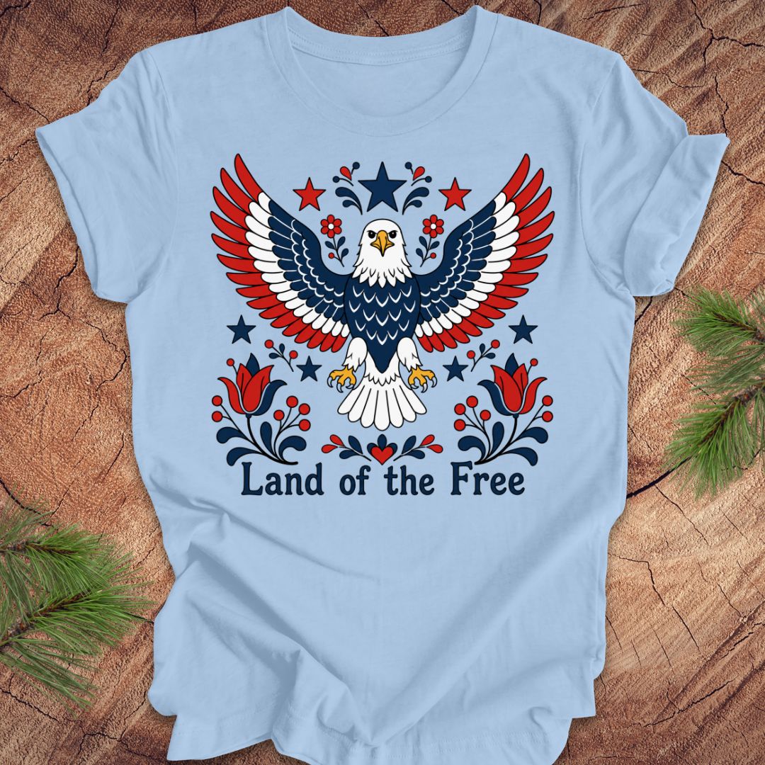 Light blue t-shirt with an eagle design and 'Land of the Free' text on a wooden surface.