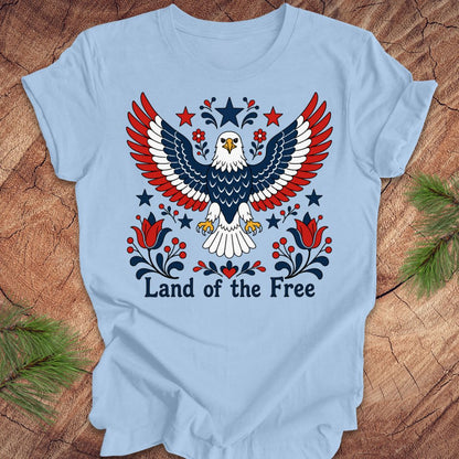 Light blue t-shirt with an eagle design and 'Land of the Free' text on a wooden surface.