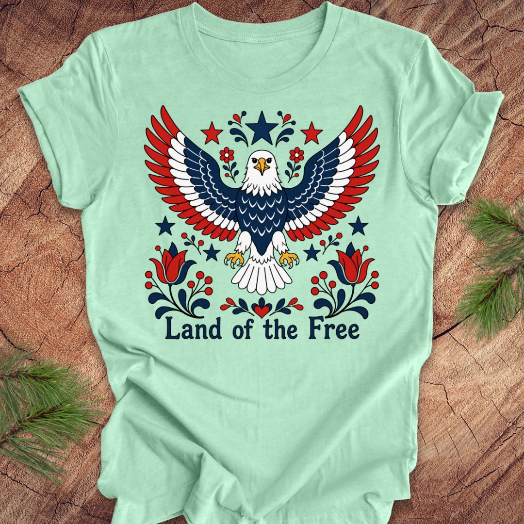 Light green t-shirt with an eagle design and 'Land of the Free' text on a wooden surface.