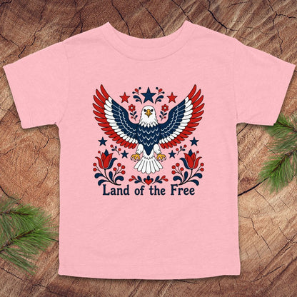 Pink t-shirt with an eagle design and 'Land of the Free' text on a wooden surface.