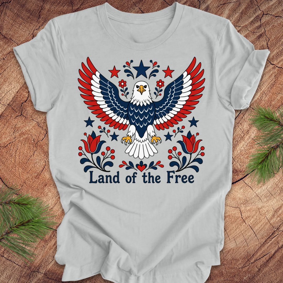 Gray t-shirt with an eagle design and 'Land of the Free' text on a wooden surface.