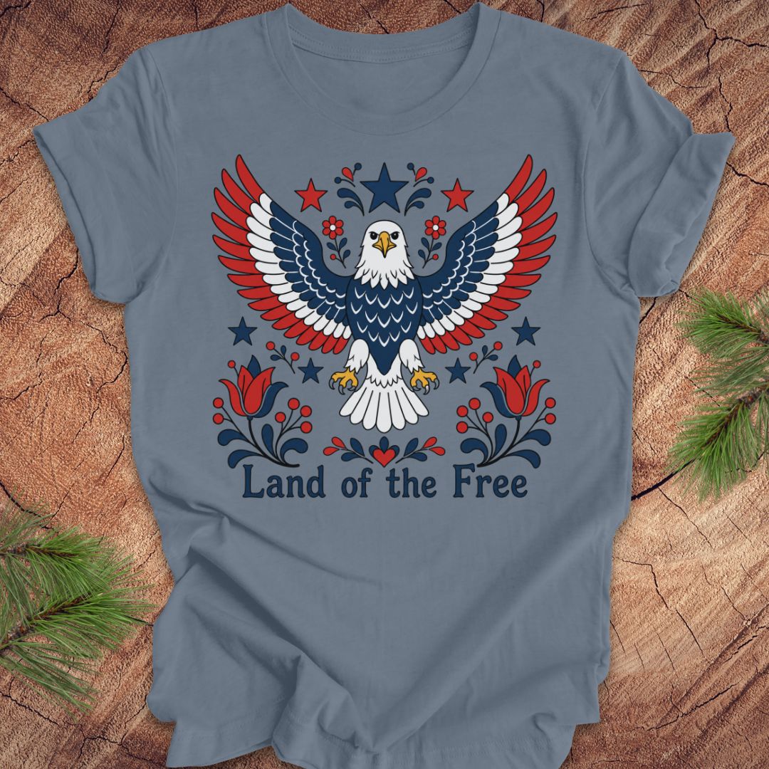 Blue t-shirt with an eagle design and 'Land of the Free' text on a wooden surface.