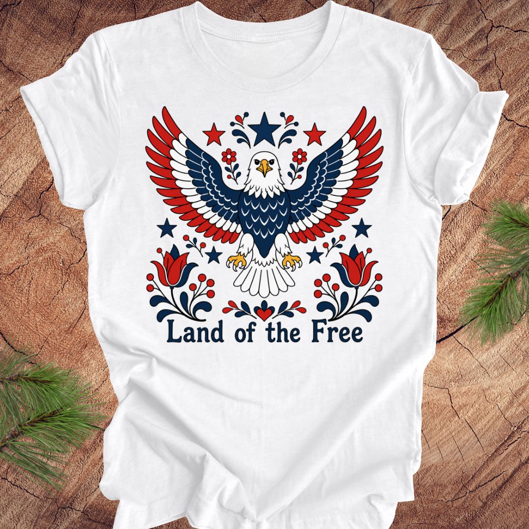 White t-shirt with an eagle design and 'Land of the Free' text on a wooden surface.