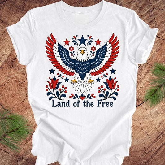 White t-shirt with an eagle design and 'Land of the Free' text on a wooden surface.