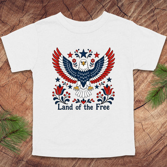 White t-shirt with an eagle design and 'Land of the Free' text on a wooden surface.