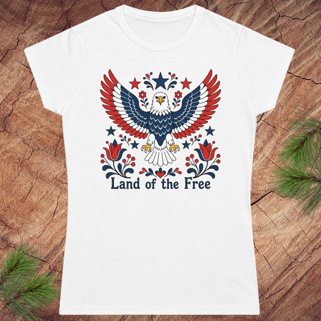White t-shirt with an eagle design and 'Land of the Free' text on a wooden surface.
