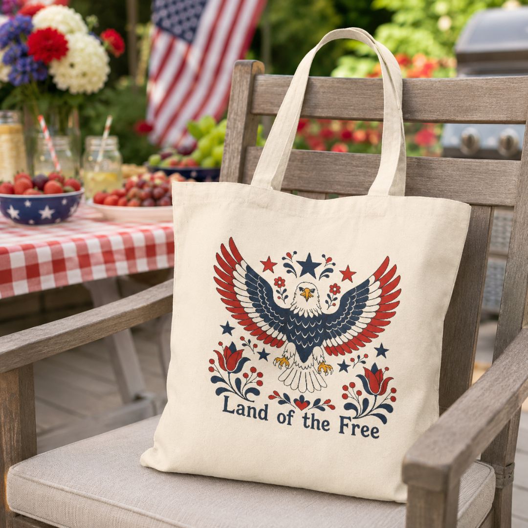 Tote bag with eagle design and 'Land of the Free' text on a chair outdoors.