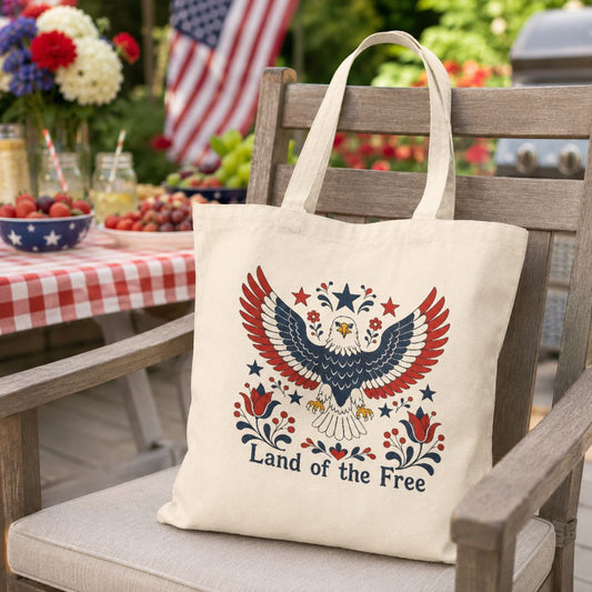 Tote bag with eagle design and 'Land of the Free' text on a chair outdoors.