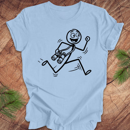 Light blue t-shirt with a stick figure design running with binoculars on a wooden surface