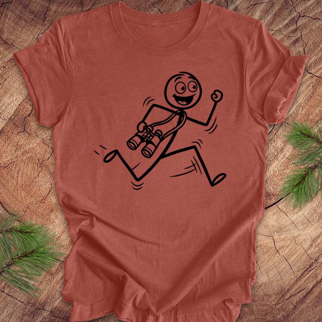 Clay colored t-shirt with a stick figure design running with binoculars on a wooden surface