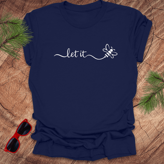 Navy blue t-shirt with 'let it' and a bee design on a wooden surface with sunglasses and pine branches.