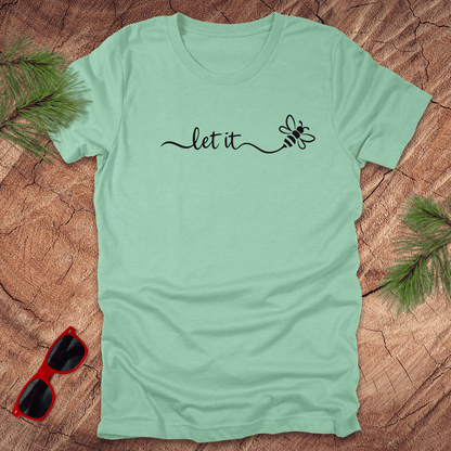 mint green t-shirt with 'let it' text on a wooden surface with sunglasses and greenery.