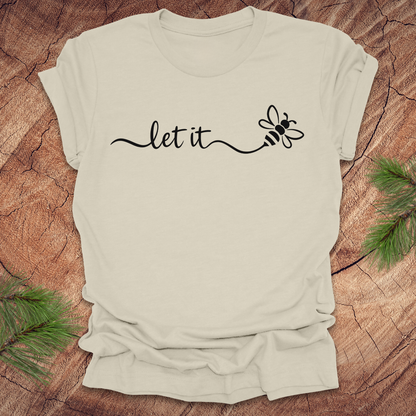 Beige t-shirt with 'let it' and bee design on a wooden surface