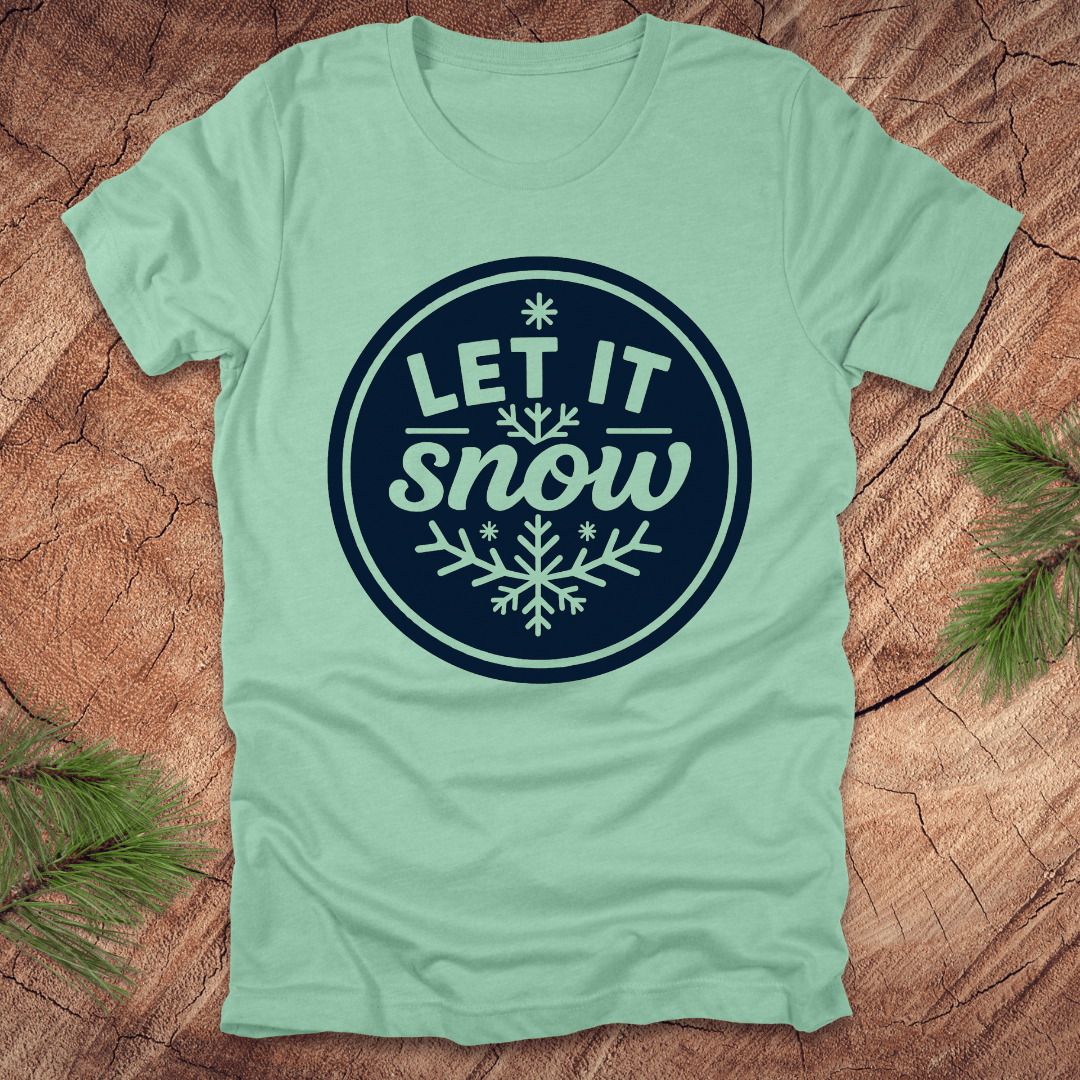 Mint green t-shirt with 'Let It Snow' design on a wooden surface