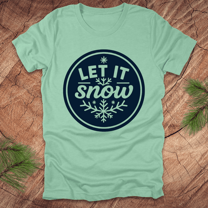 Mint green t-shirt with 'Let It Snow' design on a wooden surface