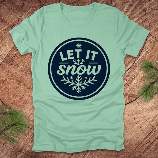 Mint green t-shirt with 'Let It Snow' design on a wooden surface