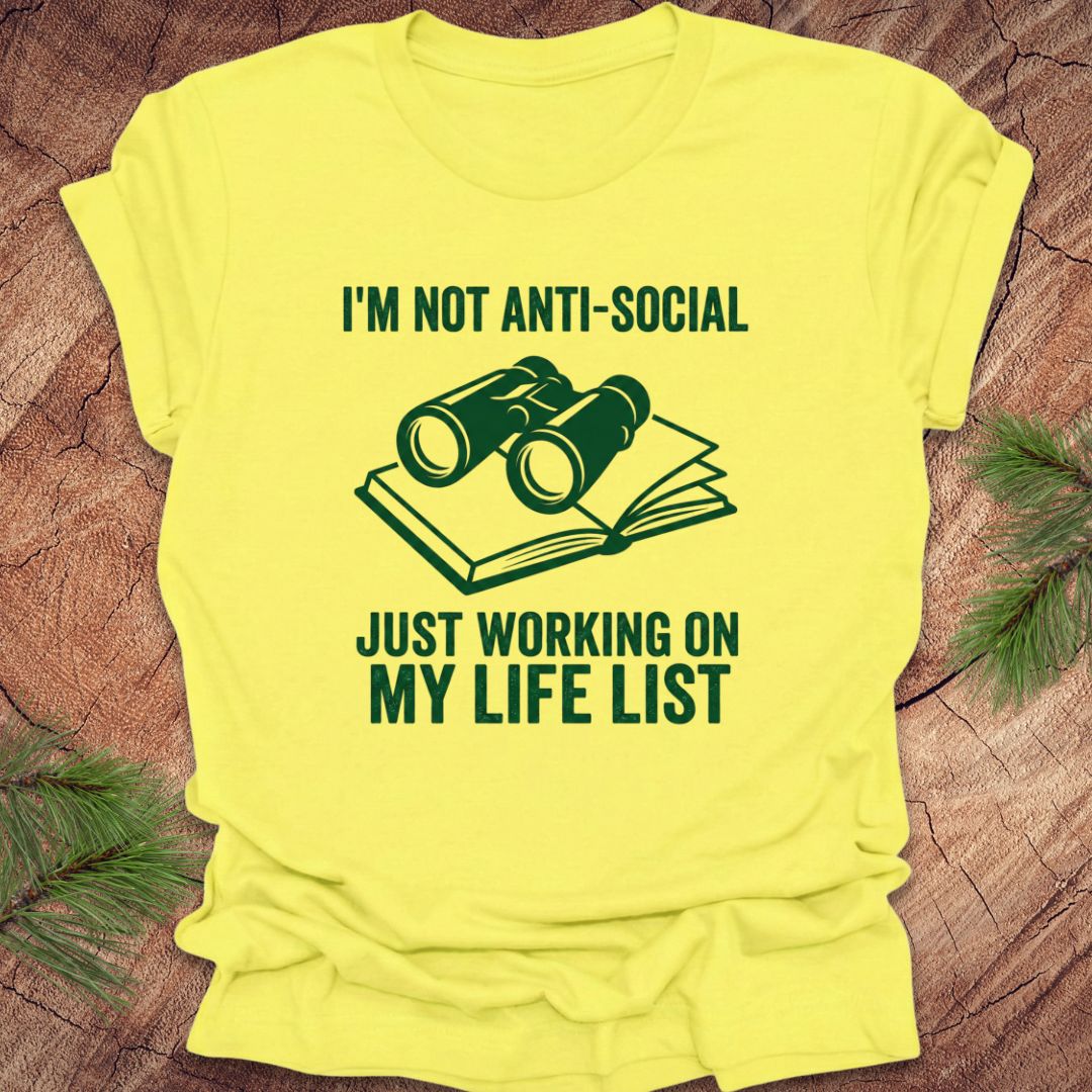 Yellow t-shirt with green text and binoculars graphic on a wooden surface