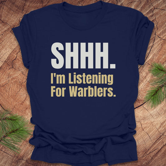 Navy blue t-shirt with text 'SHHH. I'm Listening For Warblers.' on a wooden surface.