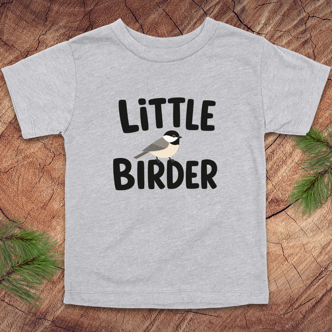 Gray t-shirt with 'Little Birder' text and a bird illustration on a wooden surface.