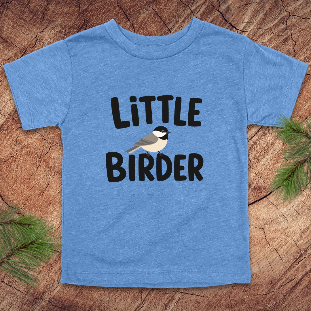 Blue t-shirt with 'Little Birder' text and a bird illustration on a wooden surface.