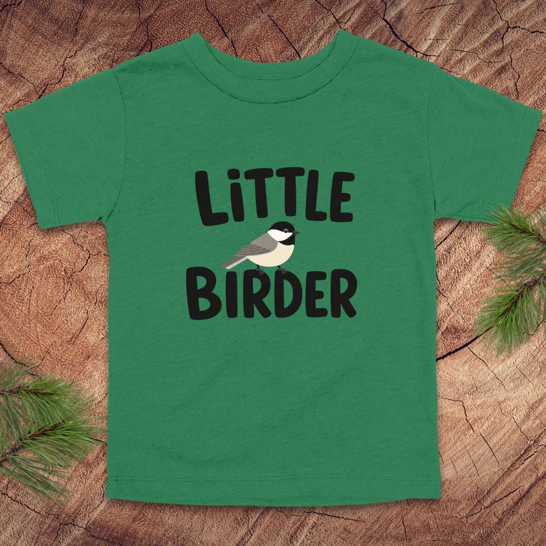 Green t-shirt with 'Little Birder' text and a bird illustration on a wooden surface.