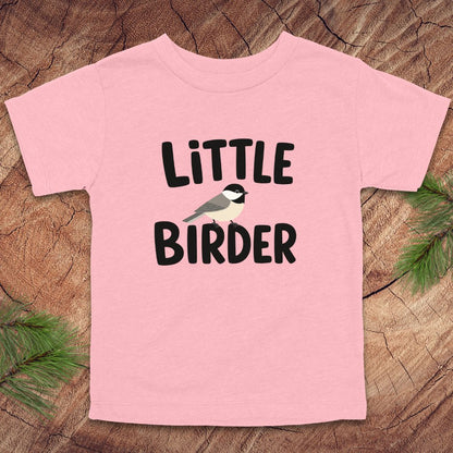 Pink t-shirt with 'Little Birder' text and a bird illustration on a wooden surface.