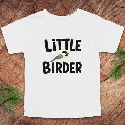 White t-shirt with 'Little Birder' text and a bird illustration on a wooden surface.