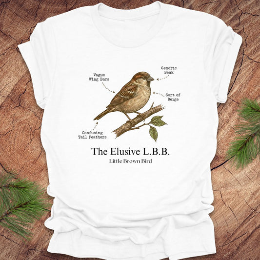 White t-shirt with a bird illustration and text 'the elusive L.B.B" on a wooden surface