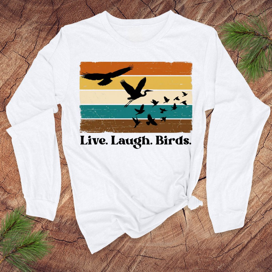 White long-sleeve shirt with bird graphic and 'Live. Laugh. Birds.' text on a wooden surface.