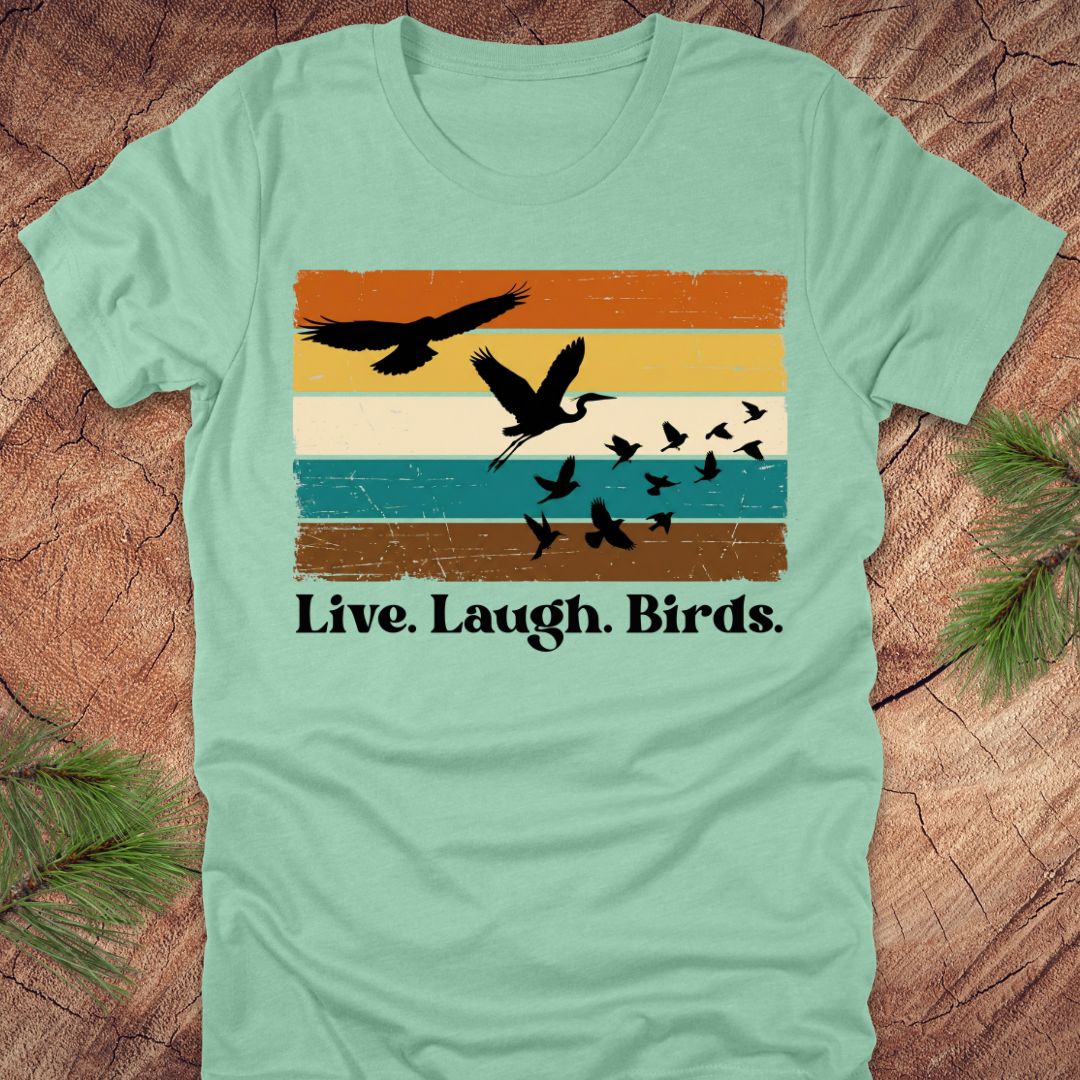 Light green t-shirt with bird graphic and 'Live. Laugh. Birds.' text on a wooden surface.