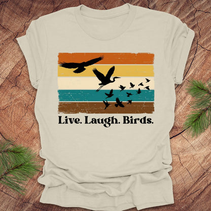 Beige t-shirt with bird design and 'Live. Laugh. Birds.' text on a wooden surface.