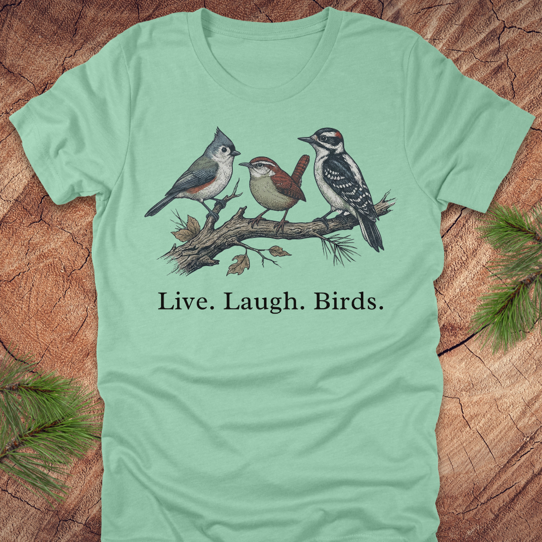 Light green t-shirt with bird illustration and 'Live. Laugh. Birds.' text on a wooden surface.