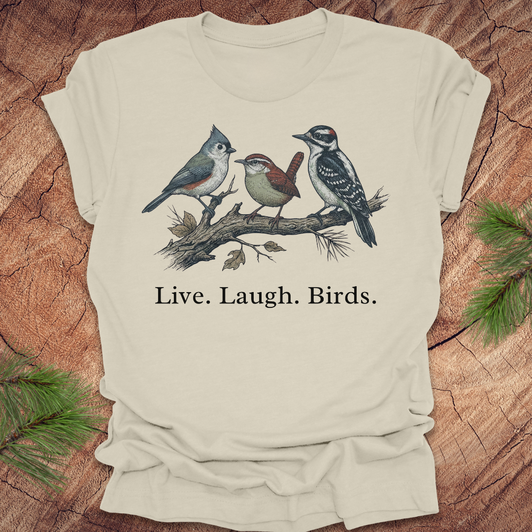 Beige t-shirt with bird illustration and 'Live. Laugh. Birds.' text on a wooden surface.