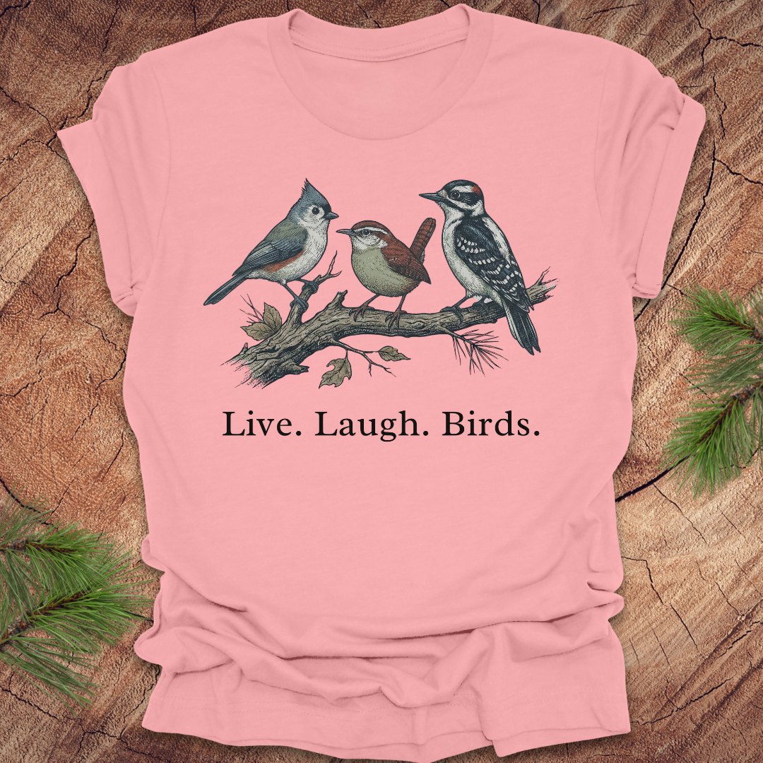 Pink t-shirt with bird design and 'Live. Laugh. Birds.' text on a wooden surface.