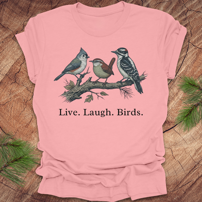 Pink t-shirt with bird design and 'Live. Laugh. Birds.' text on a wooden surface.