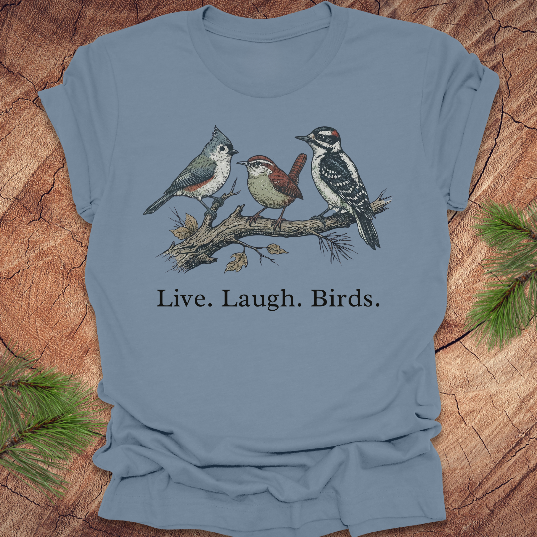 Blue t-shirt with bird illustration and 'Live. Laugh. Birds.' text on a wooden surface.