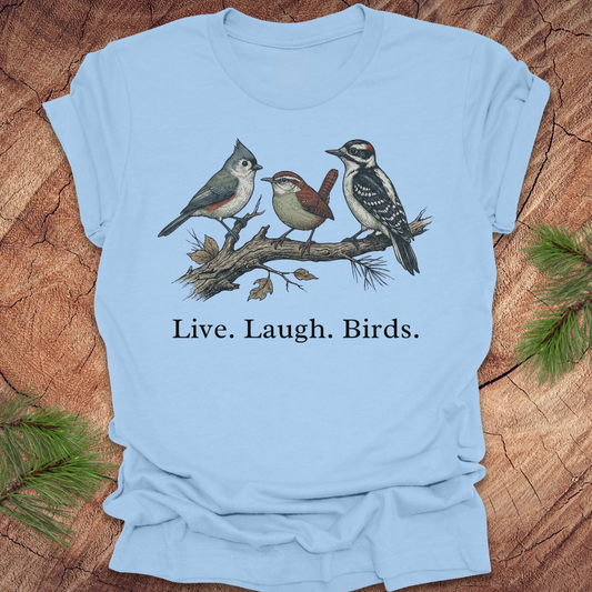 Light blue t-shirt with bird illustration and 'Live. Laugh. Birds.' text on a wooden surface.