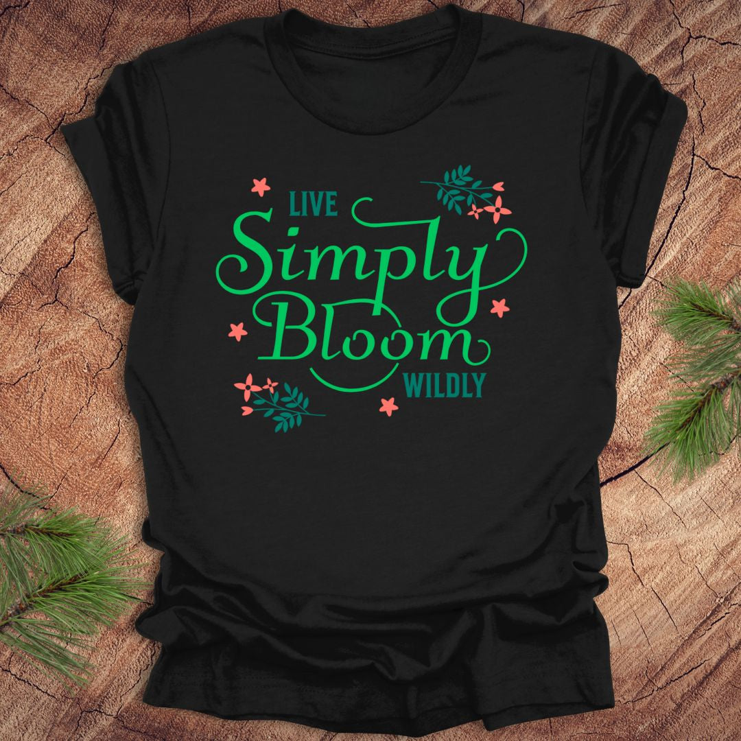 Black t-shirt with 'Live Simply Bloom Wildly' text on a wooden surface with greenery.