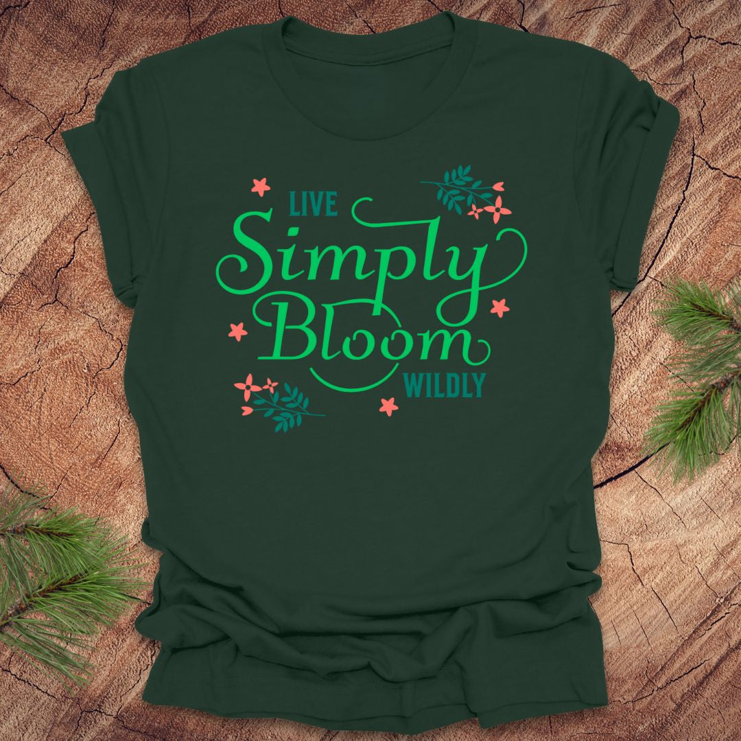 Green t-shirt with 'Live Simply Bloom Wildly' text on a wooden surface with pine branches.